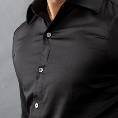 Close-up of a black natural mother‑of‑pearl button-up shirt on a gray background