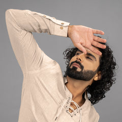 Man with beard and curly hair wearing a beige shirt against a grey background