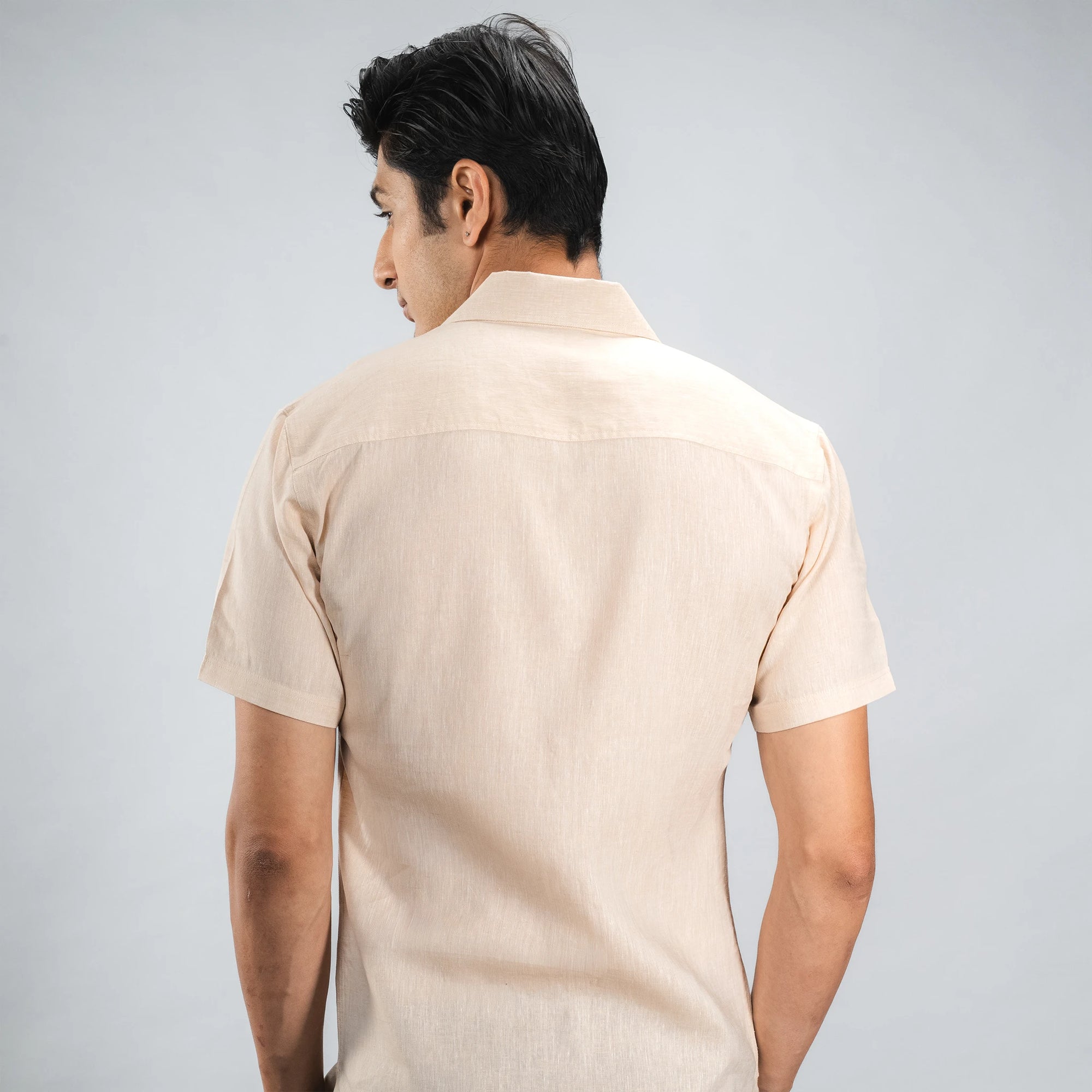 Man posing backward  wearing a beige short-sleeve shirt against a grey background