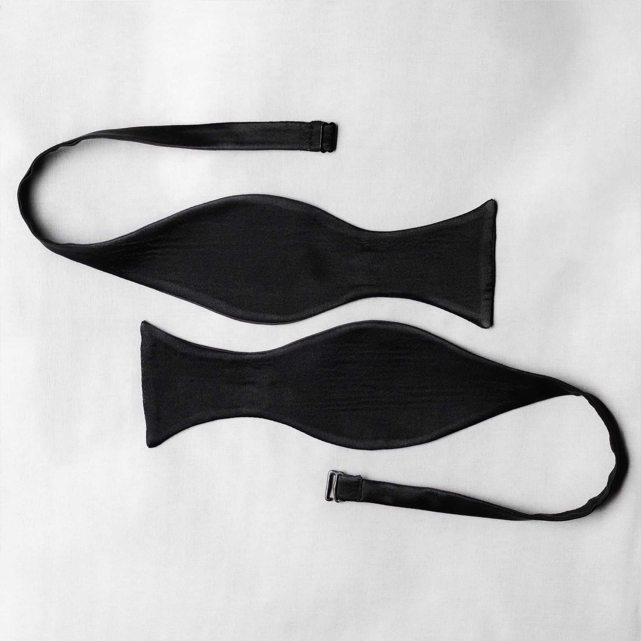 Two black satin bow tie open pieces ends curved on a white background