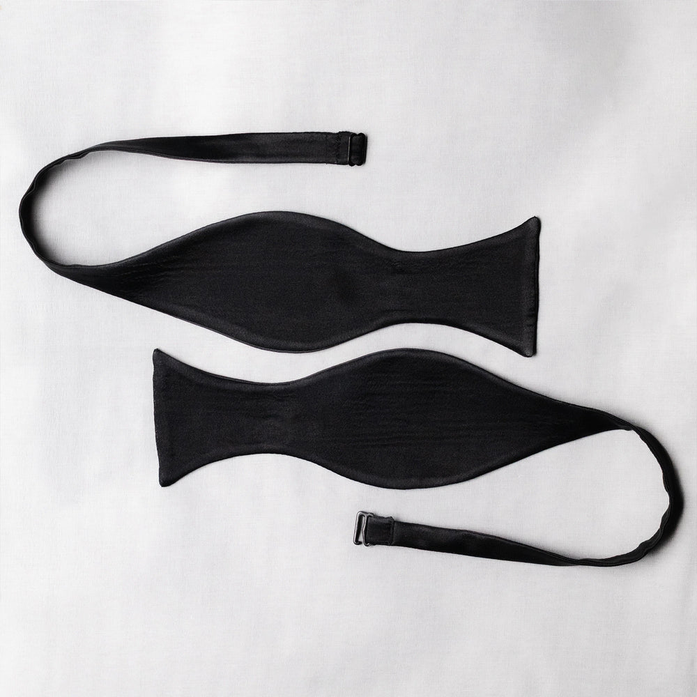 Two black satin bow tie open pieces ends curved on a white background