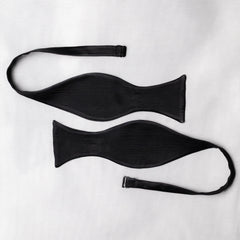 Two black satin bow tie open pieces ends curved on a white background